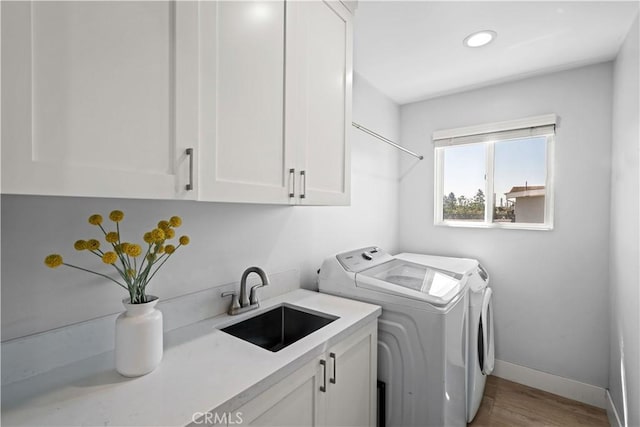 laundry room with wood finished floors, a sink, washer and dryer, cabinet space, and baseboards
