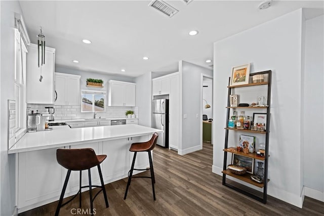kitchen with a sink, decorative backsplash, a peninsula, appliances with stainless steel finishes, and dark wood-style floors