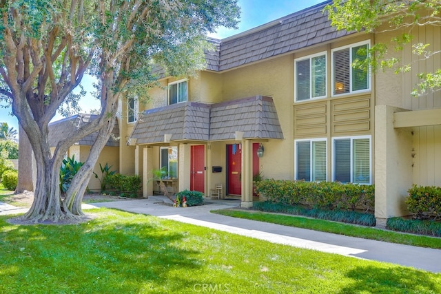 multi unit property with mansard roof, stucco siding, and a front lawn