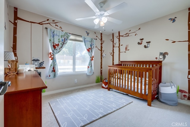 bedroom featuring baseboards, a crib, a ceiling fan, and carpet