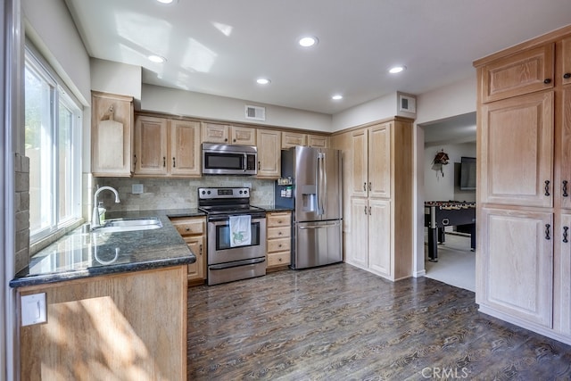 kitchen with a sink, dark wood-style flooring, stainless steel appliances, light brown cabinets, and tasteful backsplash
