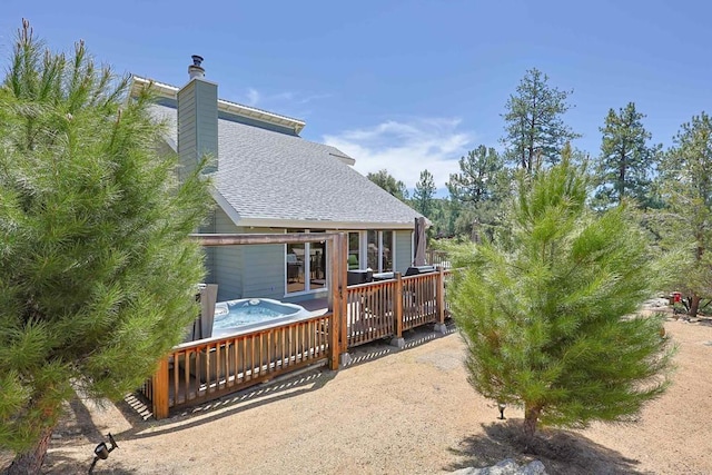 rear view of property with a hot tub, a shingled roof, a chimney, and a deck