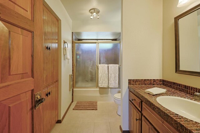 bathroom featuring vanity, tile patterned floors, enclosed tub / shower combo, and toilet