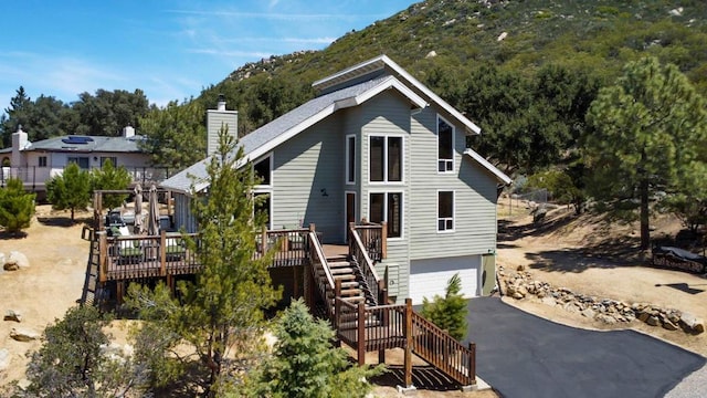 bungalow-style home with stairway, a chimney, driveway, a deck with mountain view, and a garage