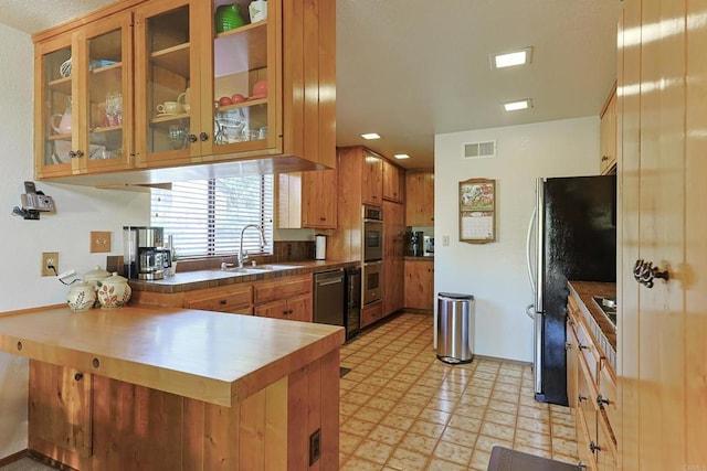 kitchen featuring a sink, light floors, stainless steel appliances, a peninsula, and visible vents