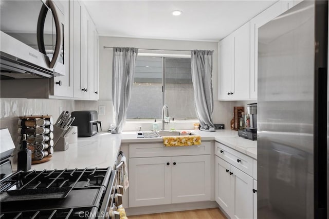 kitchen with white cabinets, a sink, recessed lighting, light stone counters, and appliances with stainless steel finishes