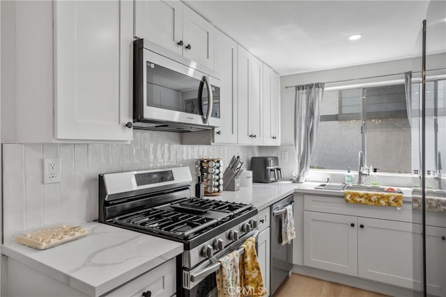 kitchen featuring white cabinets, light stone countertops, appliances with stainless steel finishes, and a sink