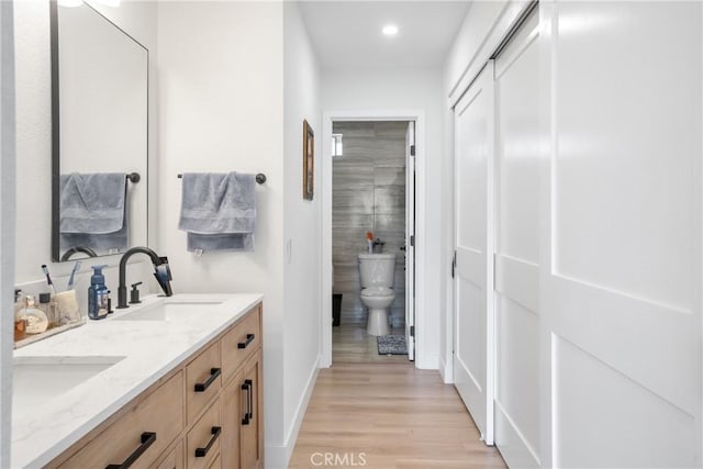 bathroom with a sink, double vanity, baseboards, recessed lighting, and wood finished floors