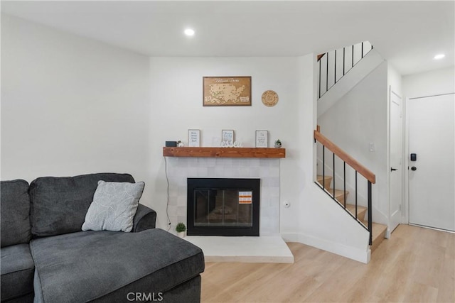 living room featuring recessed lighting, wood finished floors, a tiled fireplace, and stairway