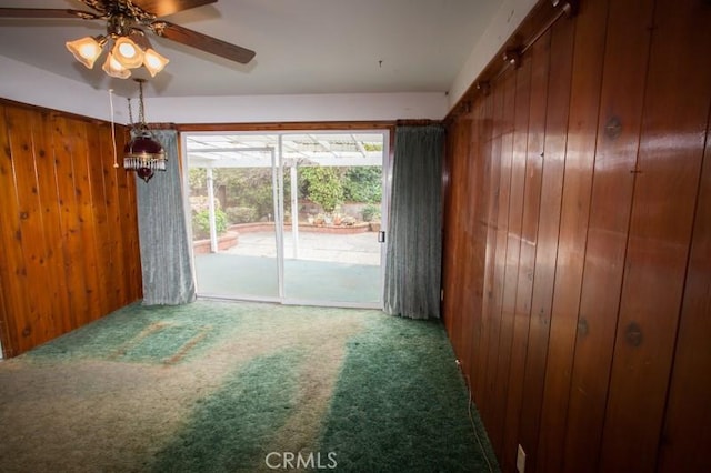 carpeted spare room featuring wooden walls and a ceiling fan