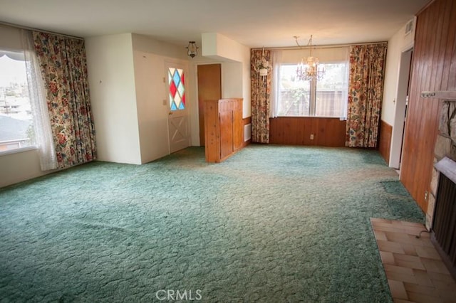 carpeted empty room with a wainscoted wall, a wealth of natural light, and a chandelier