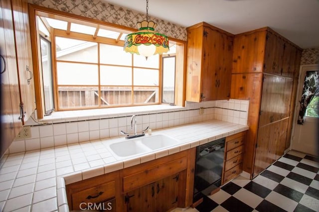 kitchen with a sink, brown cabinets, light floors, dishwasher, and decorative light fixtures