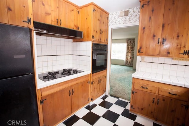 kitchen featuring tasteful backsplash, dark floors, under cabinet range hood, tile countertops, and black appliances