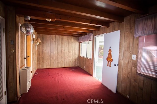 unfurnished room with beamed ceiling, carpet floors, and wood walls