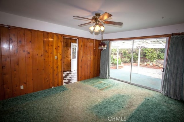 carpeted spare room with ceiling fan and wooden walls