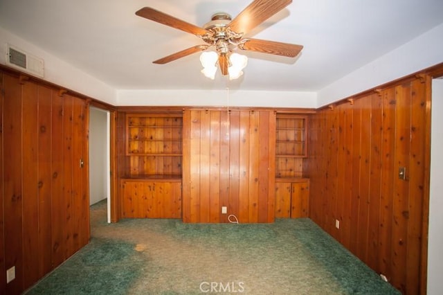 carpeted spare room with visible vents, a ceiling fan, and wood walls