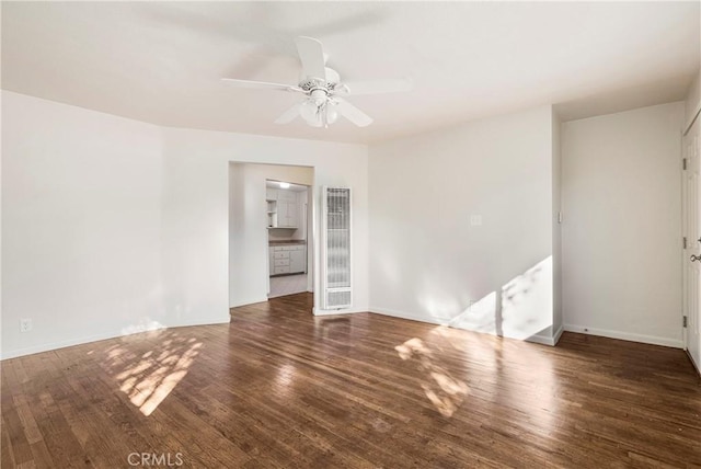 unfurnished room with baseboards, a ceiling fan, wood finished floors, and a heating unit