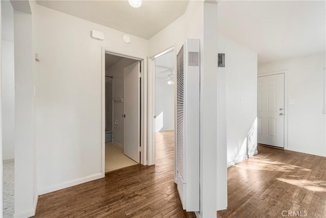 corridor with wood finished floors, baseboards, and a heating unit