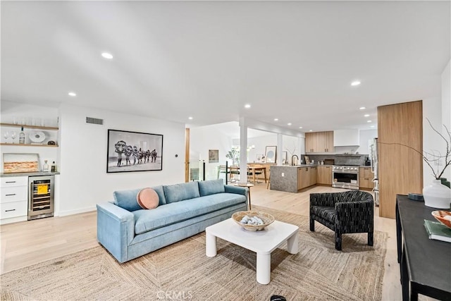 living area featuring beverage cooler, bar, light wood finished floors, visible vents, and recessed lighting
