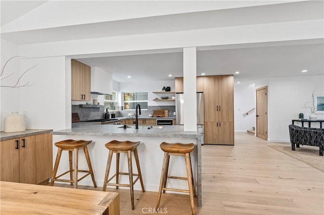 kitchen with light wood-style flooring, a sink, freestanding refrigerator, a kitchen bar, and modern cabinets