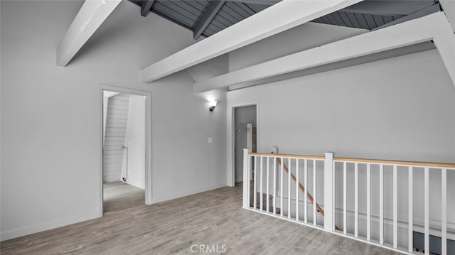 unfurnished room with wood finished floors, vaulted ceiling with beams, and baseboards