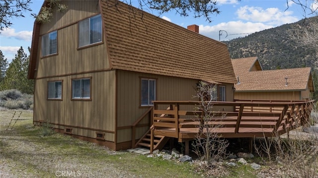 back of house featuring a deck with mountain view, roof with shingles, a gambrel roof, and a chimney