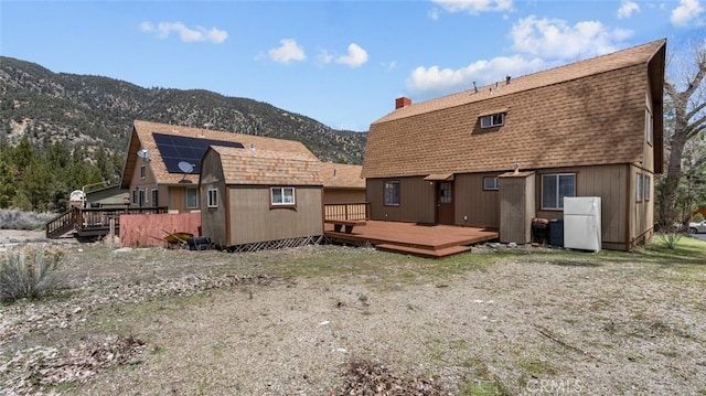 back of property with a gambrel roof, a chimney, roof with shingles, and a deck with mountain view