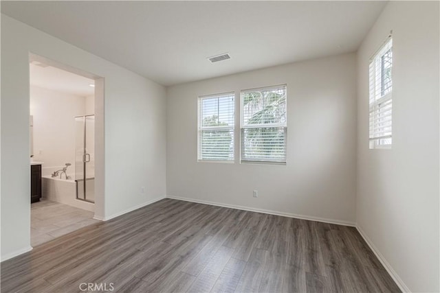 empty room featuring baseboards, plenty of natural light, wood finished floors, and visible vents