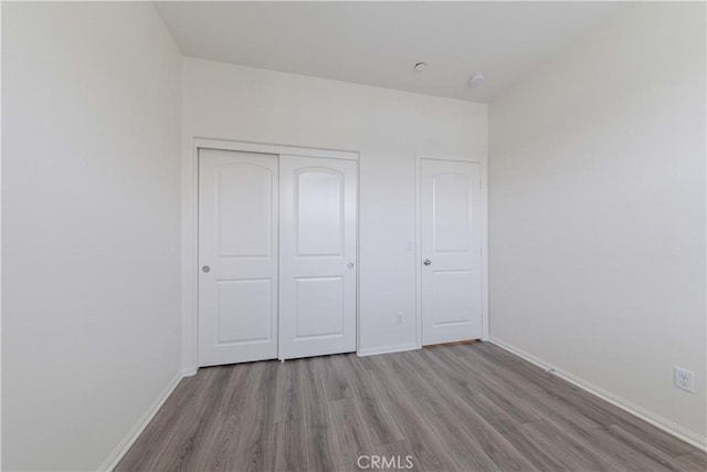 unfurnished bedroom with baseboards, wood finished floors, and a closet