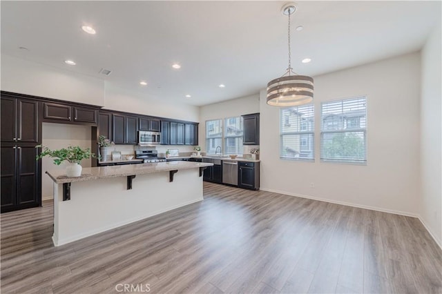 kitchen with a center island, a sink, light wood-style floors, a breakfast bar, and stainless steel appliances