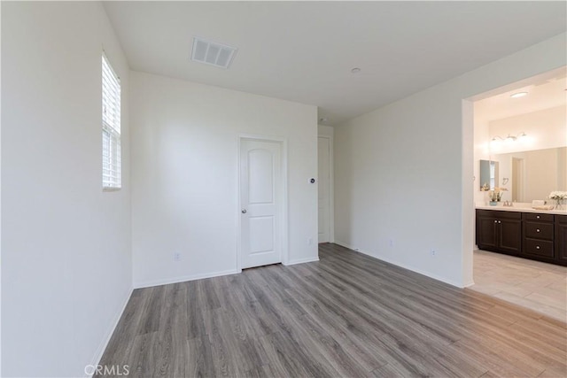 unfurnished bedroom featuring baseboards, visible vents, light wood-style flooring, and ensuite bathroom