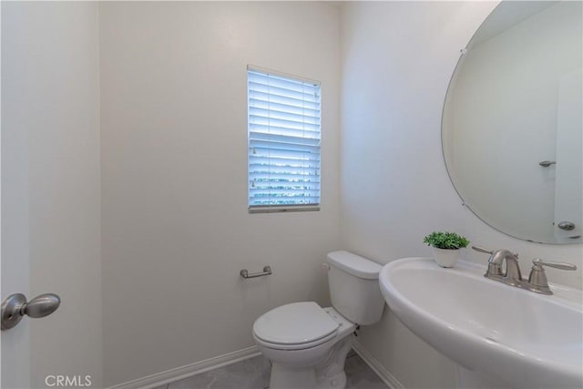 half bath with toilet, baseboards, and a sink