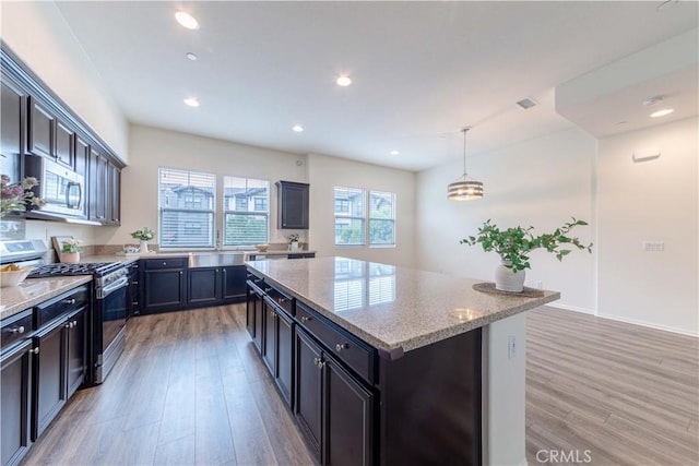 kitchen featuring a kitchen island, appliances with stainless steel finishes, light stone counters, and light wood-style floors