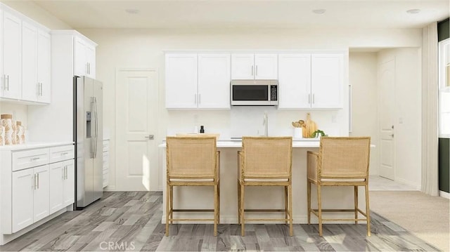 kitchen featuring white cabinetry, a kitchen bar, stainless steel microwave, refrigerator with ice dispenser, and a kitchen island