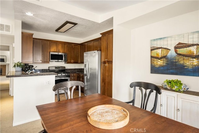 kitchen featuring visible vents, a peninsula, appliances with stainless steel finishes, and dark countertops