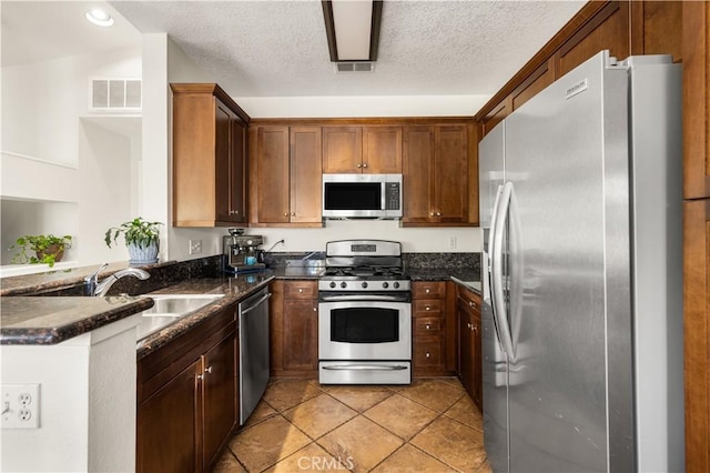 kitchen featuring a peninsula, stainless steel appliances, dark stone counters, light tile patterned flooring, and visible vents