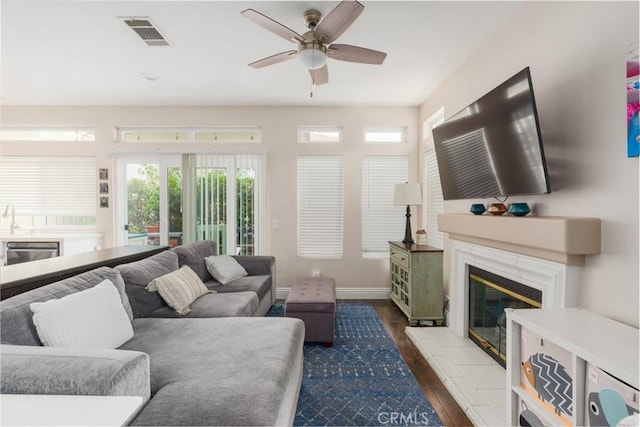 living area featuring a ceiling fan, wood finished floors, a premium fireplace, baseboards, and visible vents