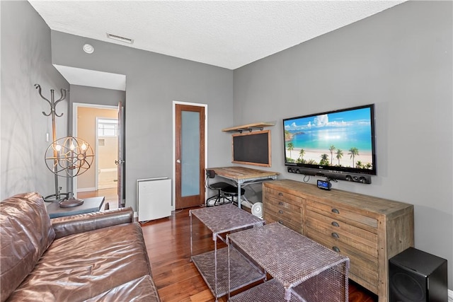 living area with a textured ceiling, visible vents, wood finished floors, and baseboards