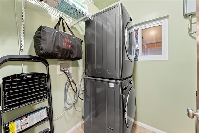 washroom featuring baseboards, stacked washing maching and dryer, tile patterned flooring, and laundry area