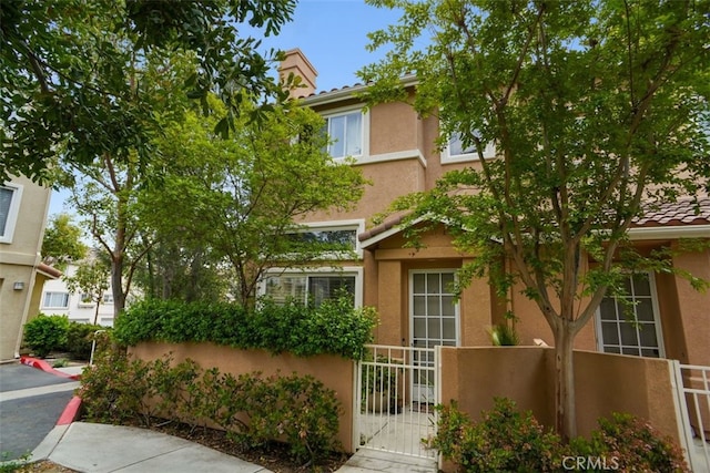 view of front facade featuring stucco siding, a gate, and fence private yard