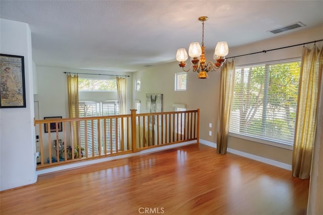 empty room with an inviting chandelier, wood finished floors, visible vents, and baseboards