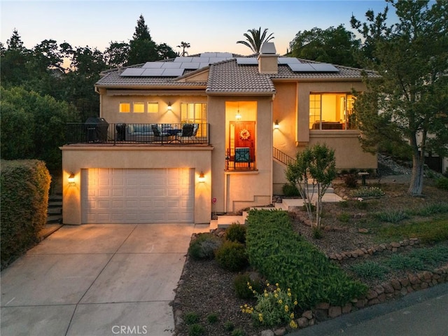 view of front of home featuring stucco siding, concrete driveway, solar panels, and a balcony