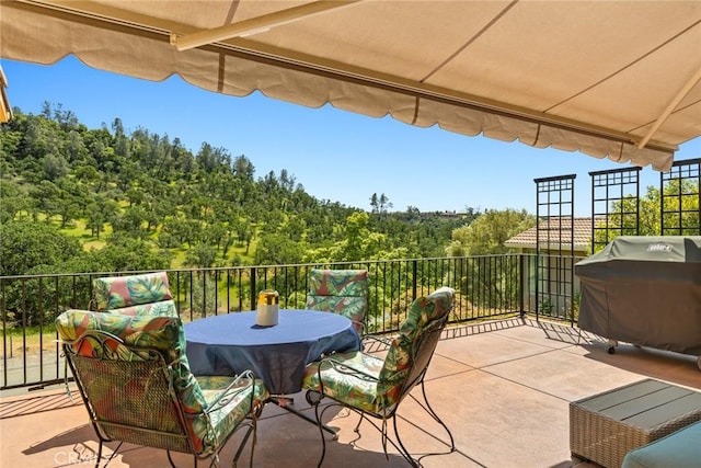 view of patio / terrace with area for grilling, a wooded view, and outdoor dining area