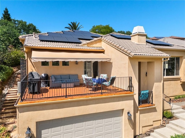 back of property with roof mounted solar panels, stairs, stucco siding, and a garage
