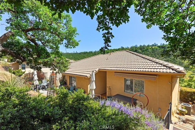 back of house with cooling unit, a tile roof, and stucco siding