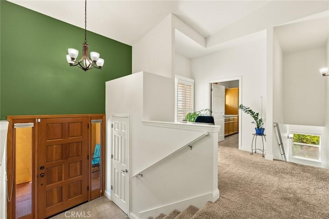 entryway featuring baseboards, a high ceiling, light colored carpet, and a notable chandelier