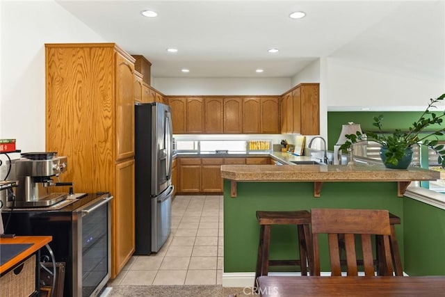 kitchen with a kitchen bar, stainless steel refrigerator with ice dispenser, a sink, a peninsula, and light tile patterned flooring
