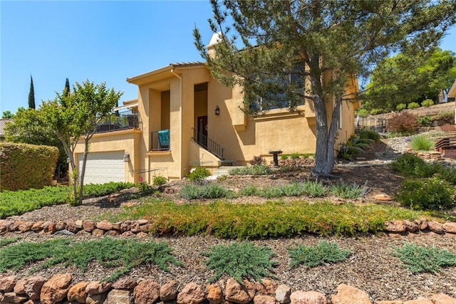 adobe home featuring a garage, stucco siding, and a balcony