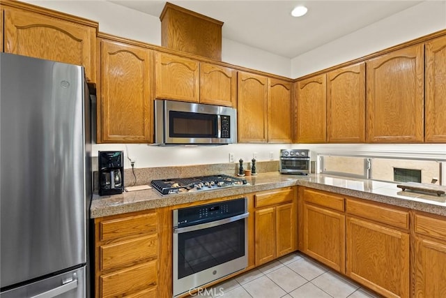 kitchen with appliances with stainless steel finishes, light tile patterned floors, and brown cabinets