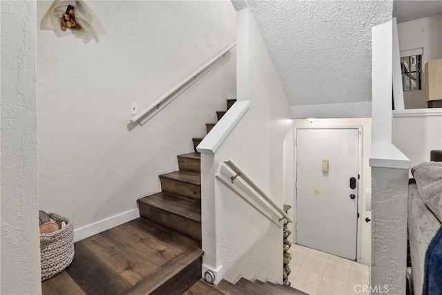 staircase featuring a textured ceiling, a textured wall, and baseboards